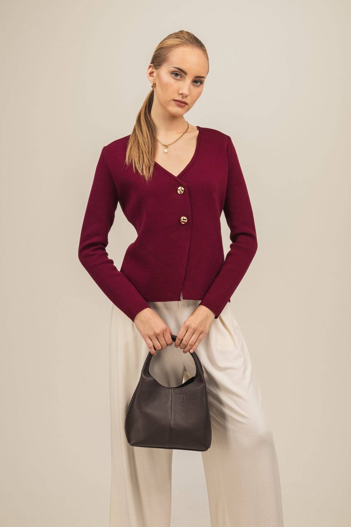 Sweter Amara – elegancki kardigan damski w kolorze bordo wystylizowany z białymi spodniamii brązową skórzaną torebką do ręki